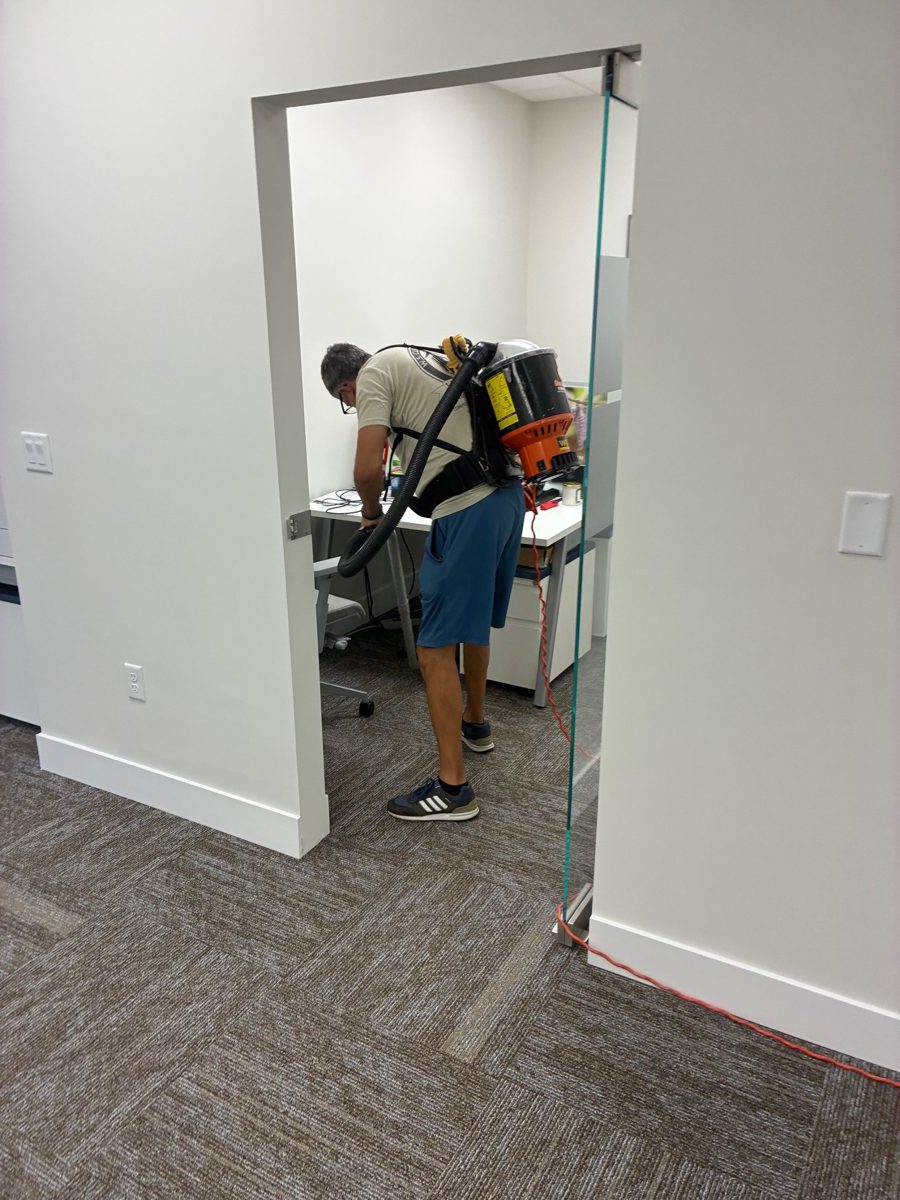 Crew member with a backpack vacuum cleaning a private office