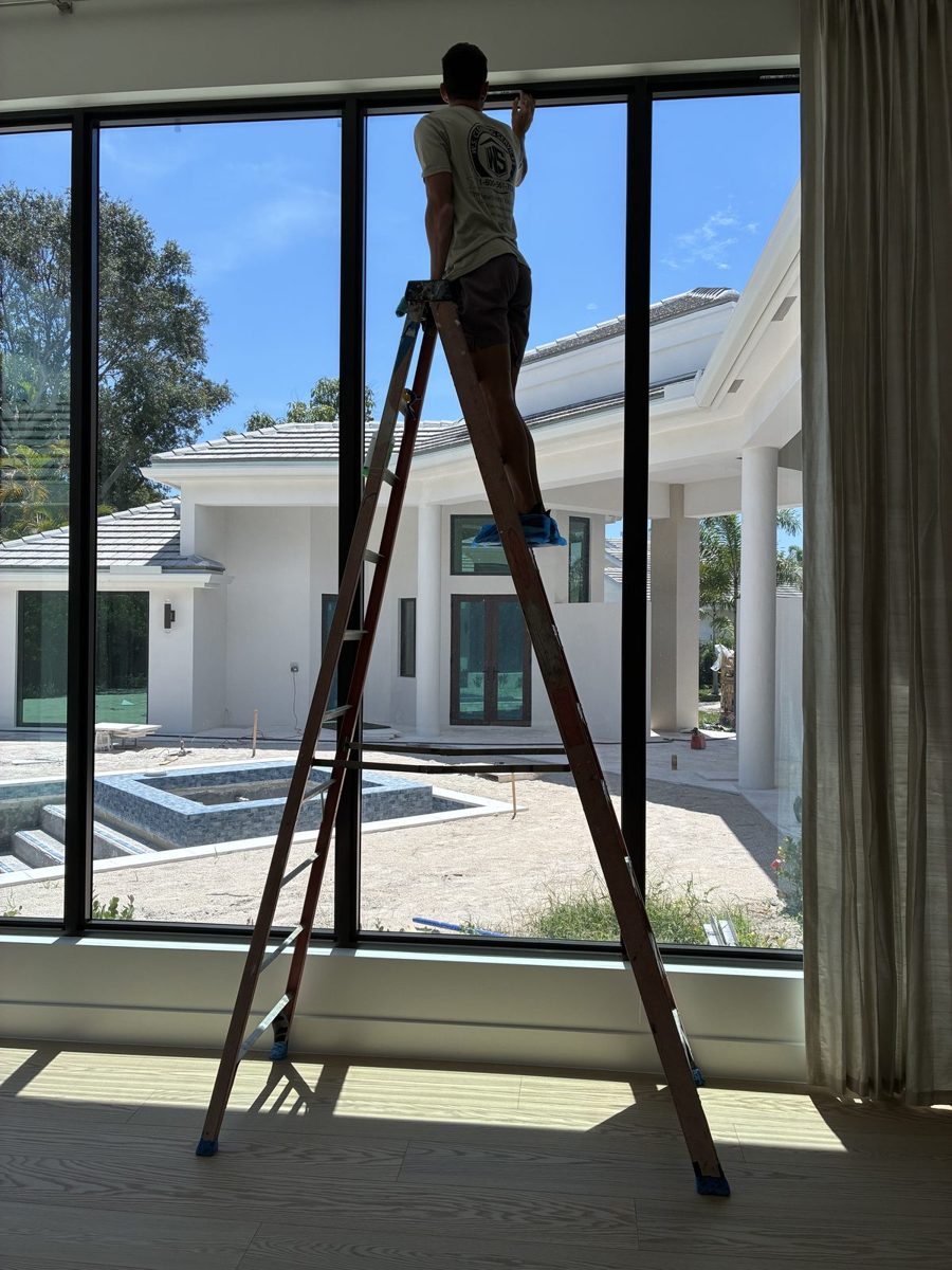 Crew member on a ladder cleaning tall interior windows on a post-construction clean